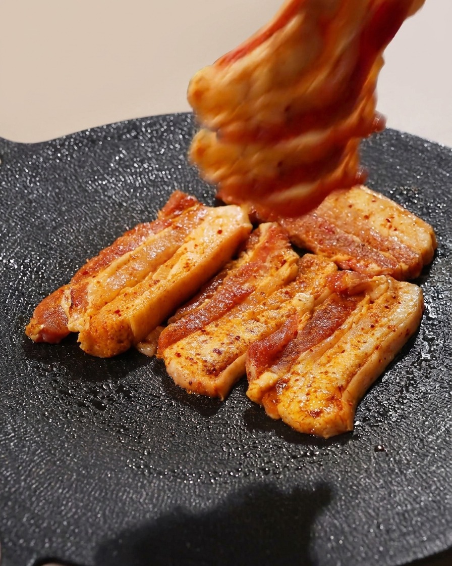 뜨거운 그릴 팬 위에 여러 줄의 삼겹살을 가지런히 배치하는 모습