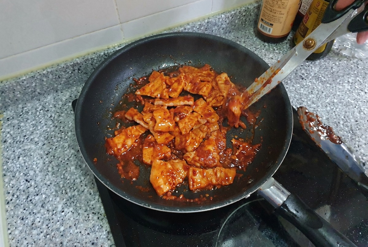 팬 안에서 윤기가 흐르며 먹음직스럽게 카라멜라이징된 삼겹살 조각들을 골고루 볶는 모습