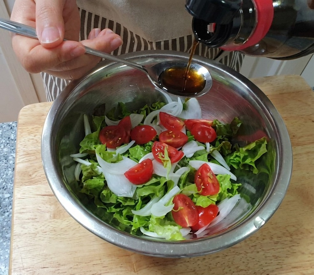 상추, 양파, 방울토마토가 담긴 볼 위로 스푼을 이용해 간장 드레싱을 뿌리는 모습