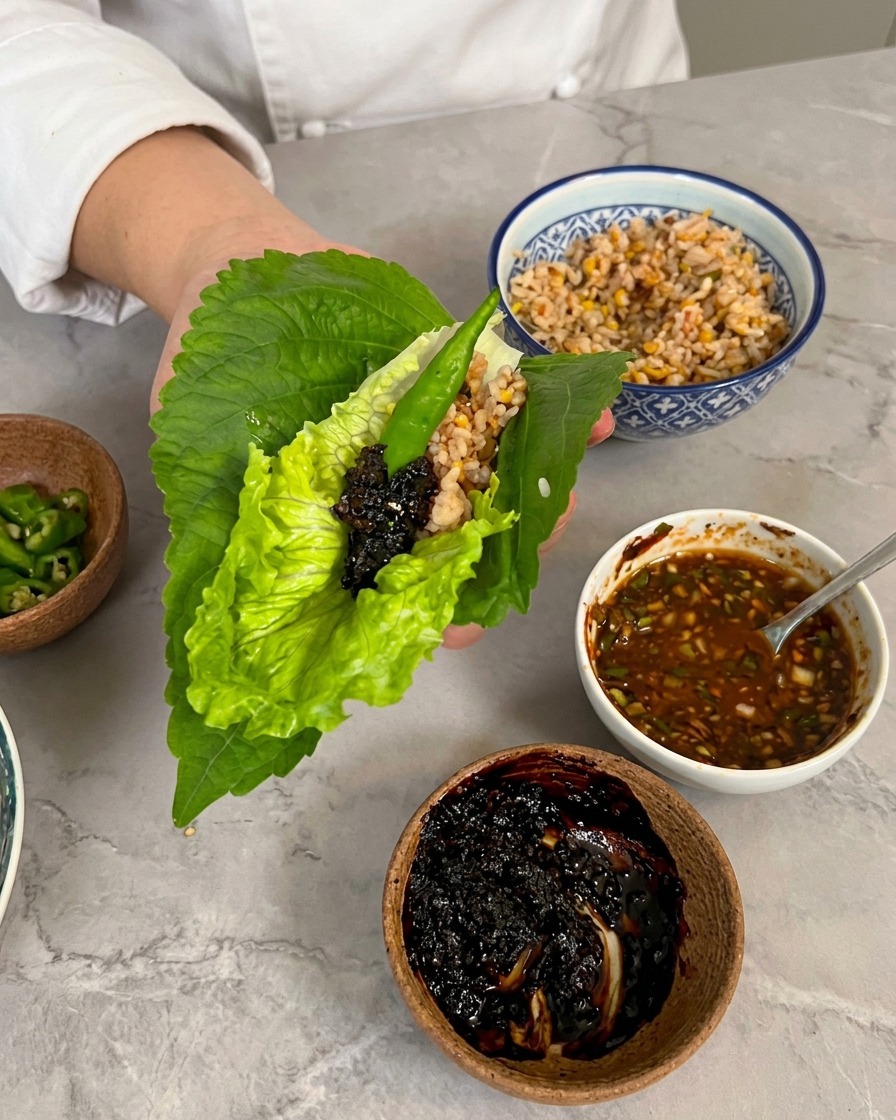 상추와 깻잎 위에 양념 소스를 얹고 청양고추를 올린 쌈을 손에 쥔 모습.