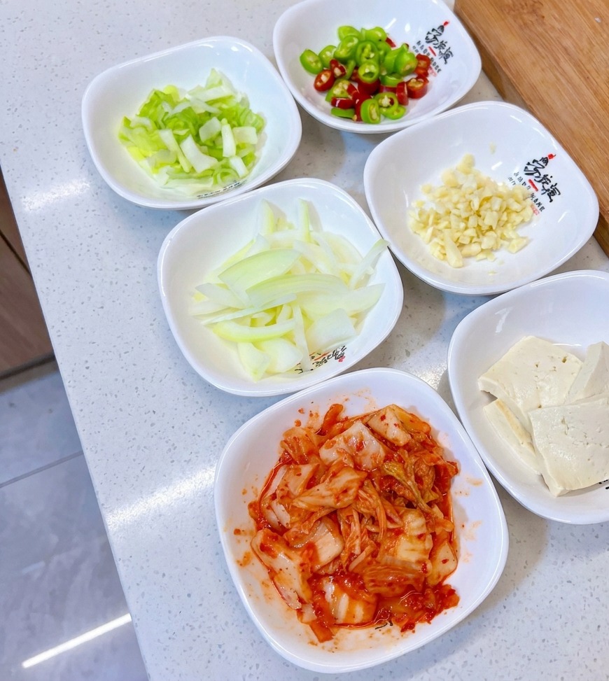 손질된 대파, 고추, 다진 마늘, 양파, 두부, 김치가 각각 작은 하얀 볼에 담겨 있는 모습