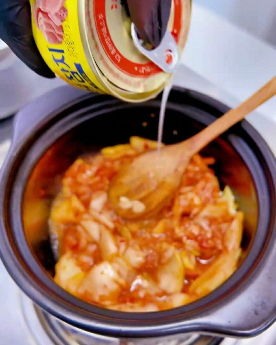 냄비 속 김치 위로 노란색 참치캔의 국물을 따라 붓는 모습