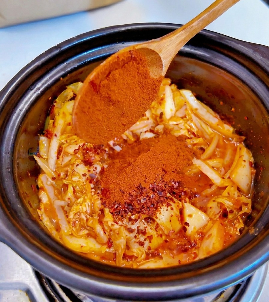 양념된 김치와 양파 위에 나무 숟가락으로 고운 고춧가루를 뿌리는 모습