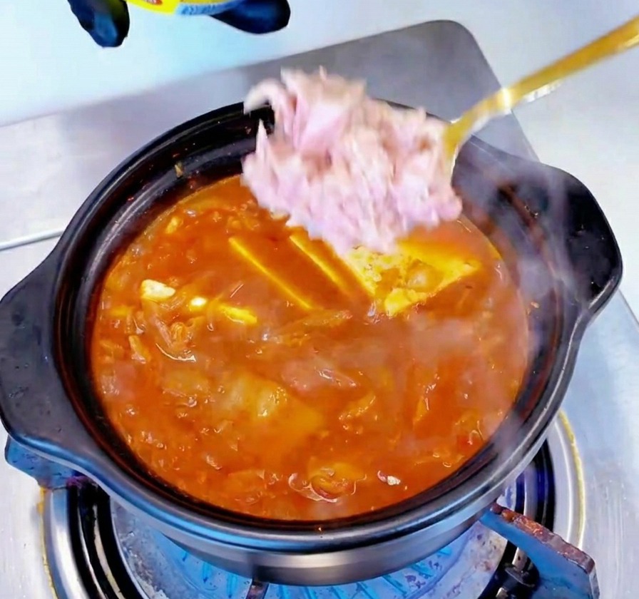 끓고 있는 붉은 찌개 한가운데로 연분홍빛 참치 살코기를 숟가락으로 떠 넣는 모습