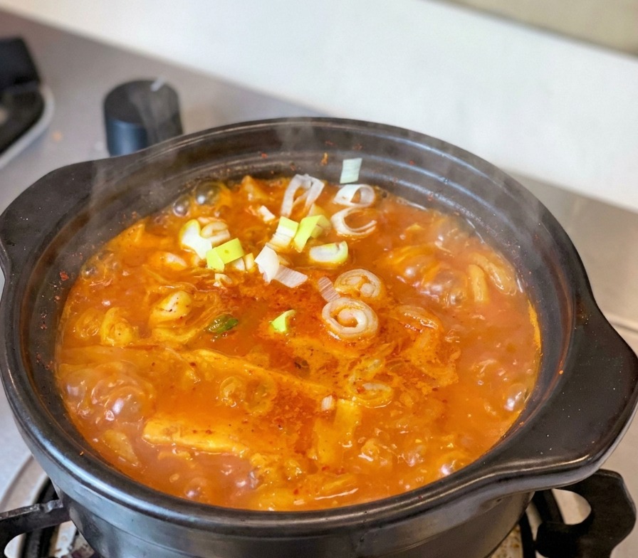 가스레인지 위 전통 뚝배기에서 보글보글 끓고 있는 참치김치찌개 위에 송송 썬 대파와 고추가 고명으로 올라간 모습