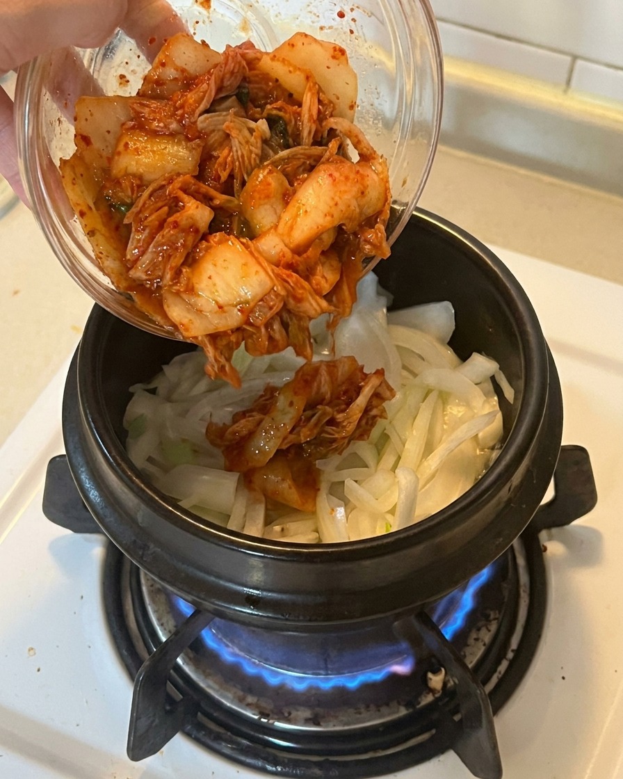 볶은 양파와 대파가 담긴 냄비에 먹기 좋게 썬 빨간 신김치를 넣는 모습