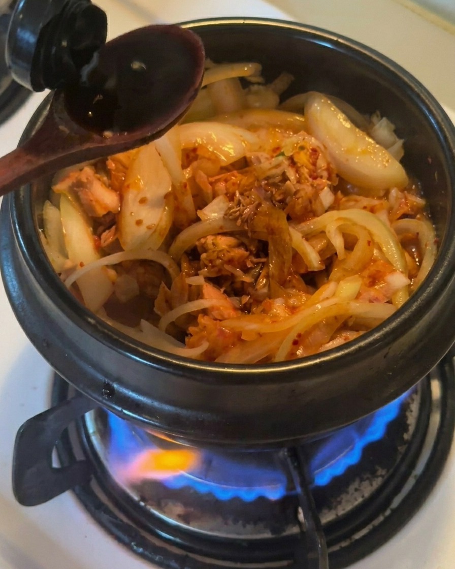 참치와 김치가 들어간 뚝배기에 나무 숟가락으로 간장을 따라 넣는 모습
