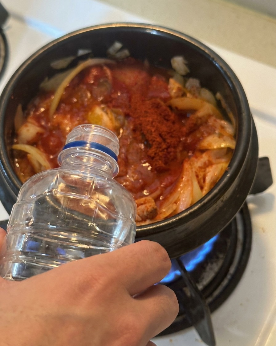 양념된 김치와 참치가 담긴 냄비에 투명한 물을 붓고 있는 모습
