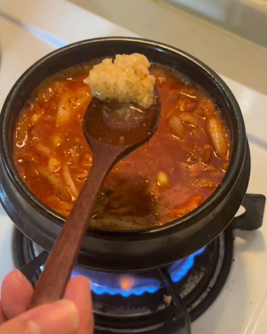 보글보글 끓고 있는 빨간 김치찌개 위로 다진 마늘 한 스푼을 넣으려는 모습