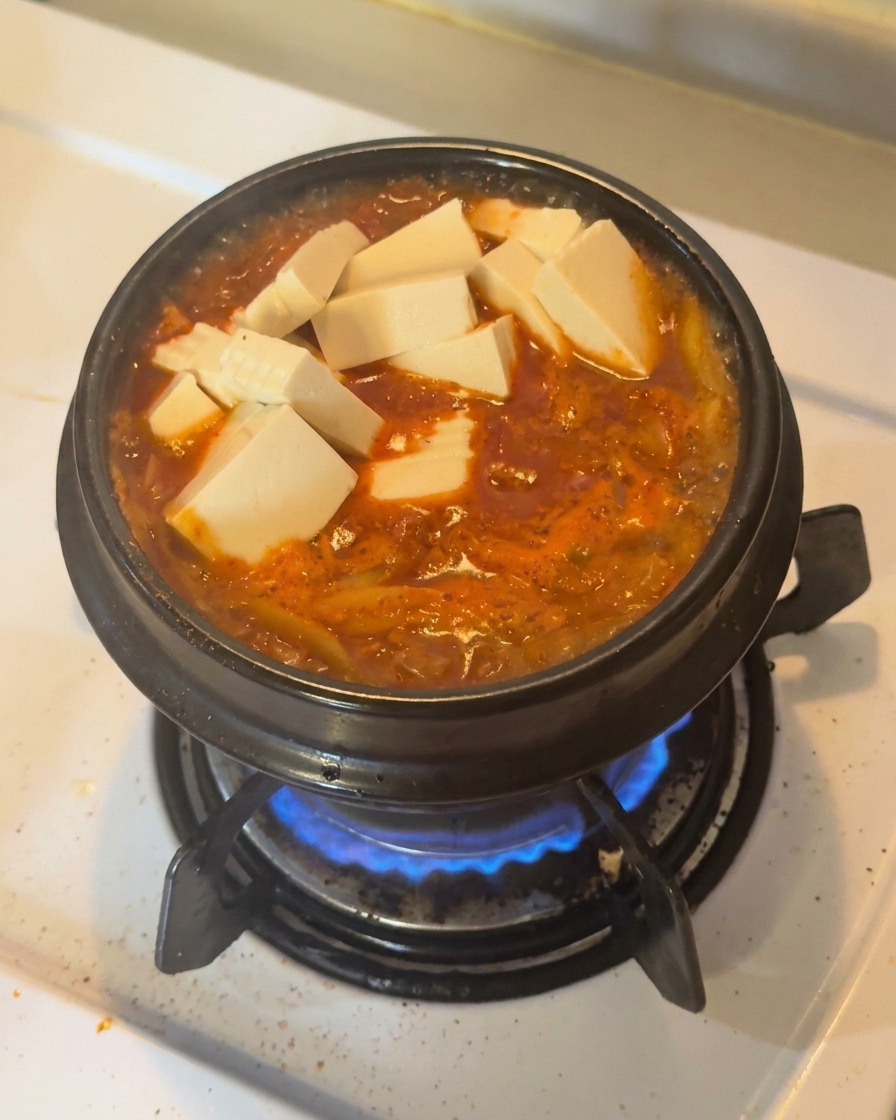보글보글 끓는 김치찌개 위에 하얀 두부와 썰어둔 청양고추를 고명으로 올린 모습