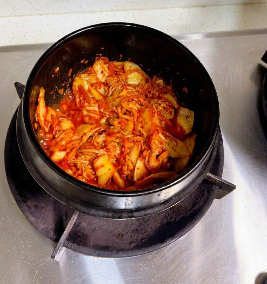 잘 볶아진 김치가 담긴 뚝배기에 뽀얀 쌀뜨물을 졸졸 붓는 손