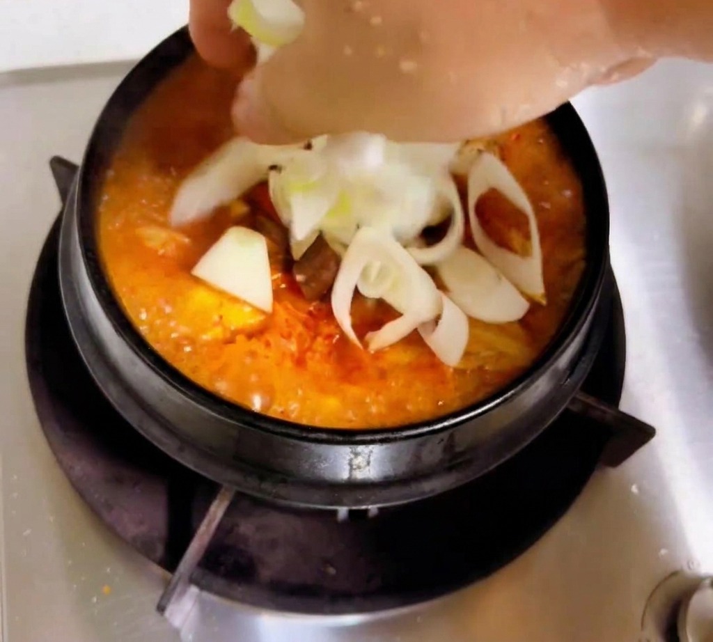 보글보글 끓는 김치찌개 위에 얇게 썬 양파, 대파, 표고버섯과 두부를 올리는 손