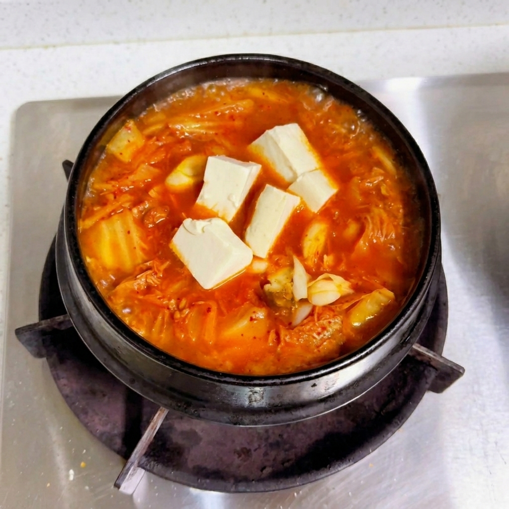 두부가 얹어진 붉은 찌개 국물에 간장과 조미료를 넣어 마무리 간을 하는 모습