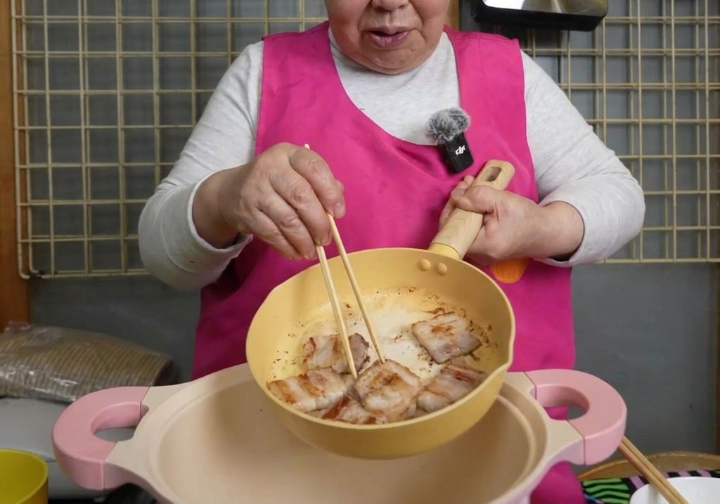젓가락을 이용해 바삭하게 구워진 삼겹살을 노란색 팬에서 큼직한 분홍색 냄비로 옮겨 담는 모습