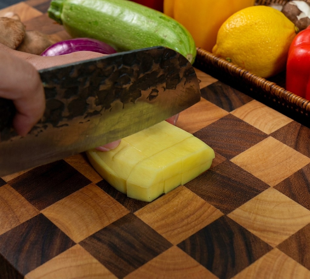 도마 위에서 껍질을 벗긴 감자를 칼로 한입 크기의 정육면체 모양으로 깍둑썰기하는 모습
