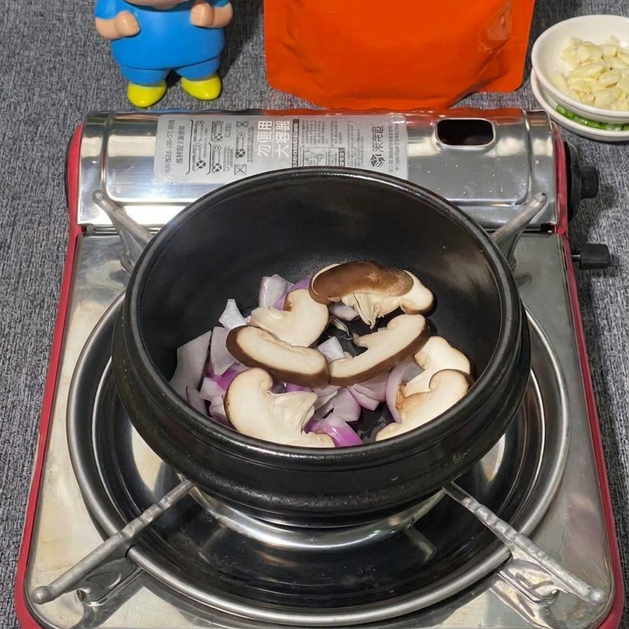 검은색 뚝배기에 담긴 적양파 위에 얇게 썬 표고버섯과 백만가닥버섯을 층층이 올리는 모습.