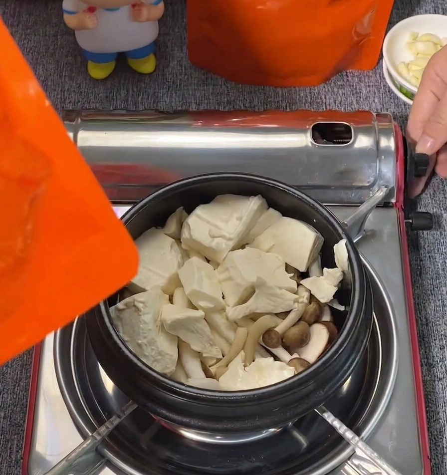 검은색 냄비 안의 버섯 위에 큼직한 순두부 덩어리가 올려진 모습.