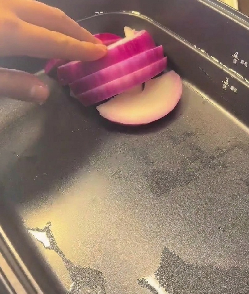 검은색 멀티쿠커 바닥에 먹기 좋게 자른 적양파를 차곡차곡 깔고 있는 손