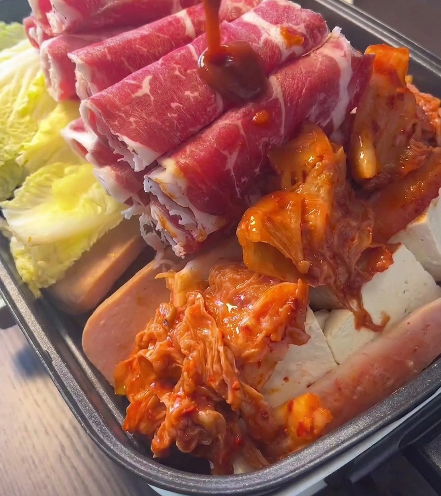 고기와 채소가 가득 찬 냄비 한가운데에 잘 익은 붉은색 김치를 듬뿍 얹은 모습