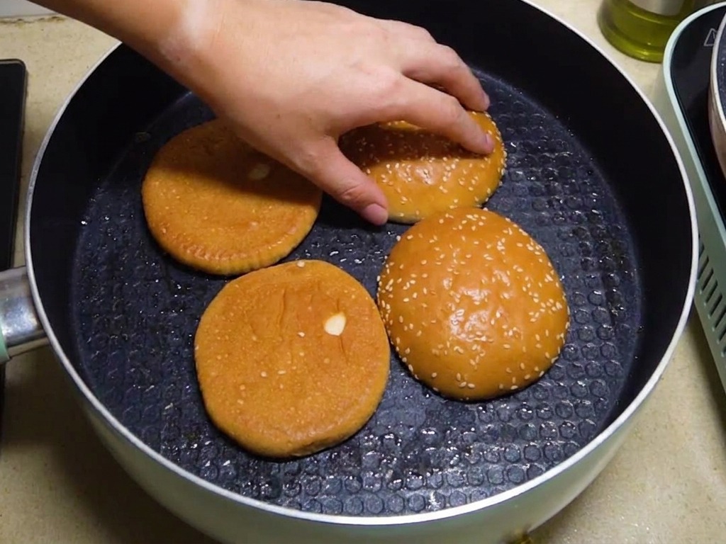 반으로 자른 버거 번 두 개를 팬에 단면이 아래로 가도록 올려 굽는 모습과 손으로 위치를 조절하는 모습.