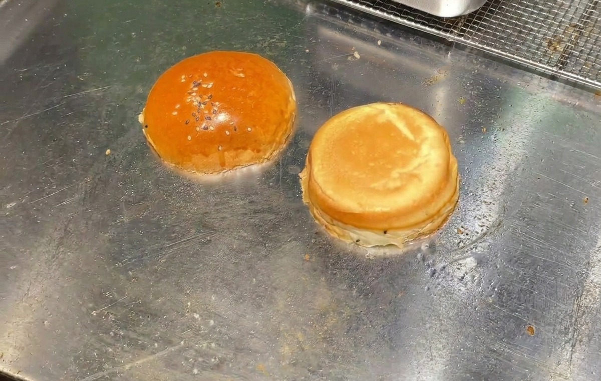 달궈진 평평한 그릴 위에 버터를 바른 버거 번 두 조각을 안쪽 면이 아래로 가도록 올려 굽는 모습.