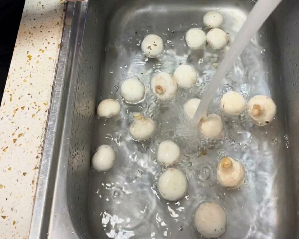 물기 있는 흰색 키친타월로 양송이버섯의 갓 부분을 부드럽게 닦아내는 손 모습