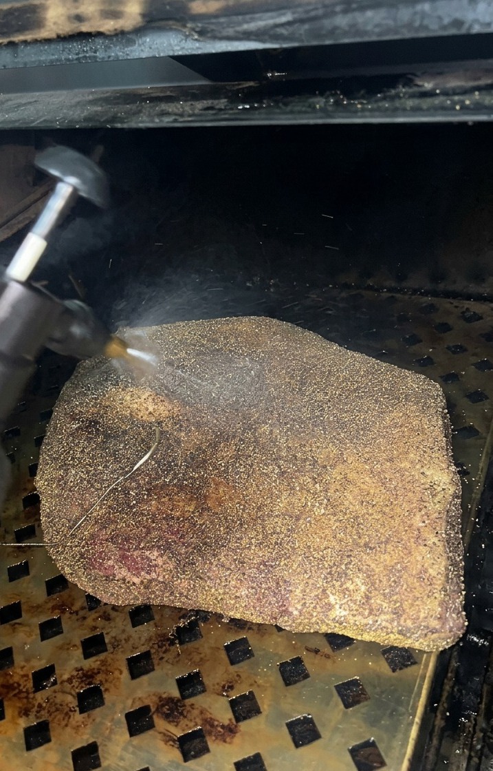 훈연기 안에서 거뭇거뭇하게 바크가 형성되고 있는 브리스킷 표면에 애플 사이더 비네거 미스트를 미세하게 분사하는 모습.