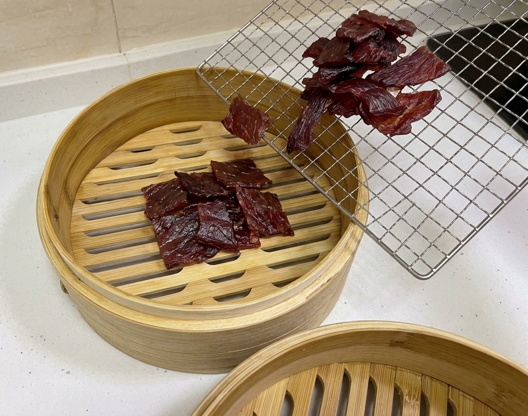 꾸덕하게 마른 진한 붉은빛의 고기를 원형 대나무 찜기 안으로 옮겨 담는 모습.