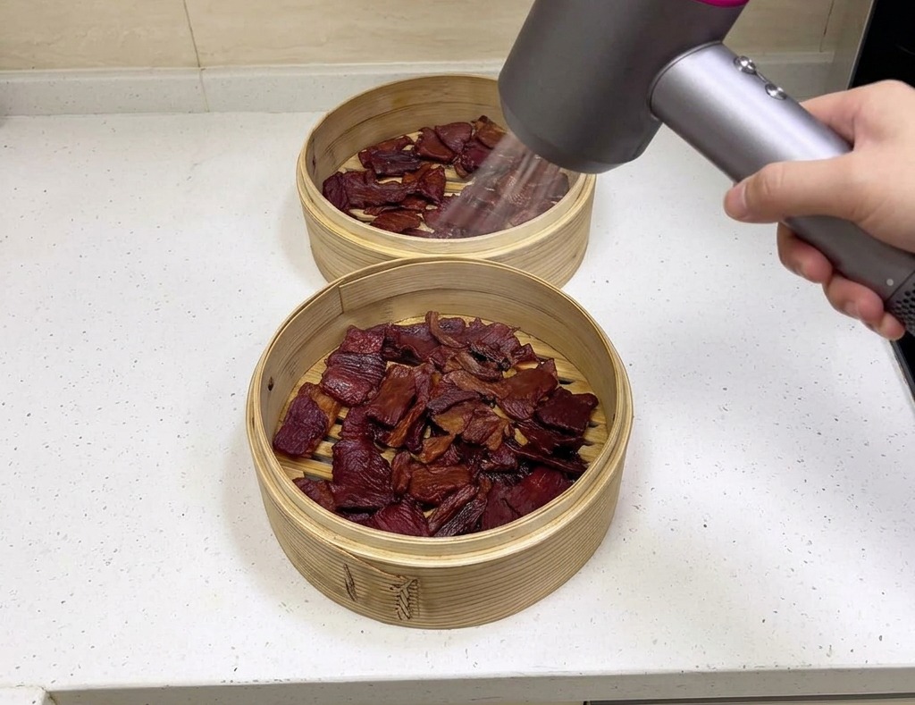 대나무 찜기에 담긴 고기 위로 헤어드라이어 바람을 쐬어 남은 수분을 날려 보내는 모습.