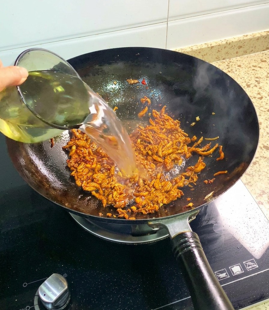 양념에 잘 볶아진 닭고기가 담긴 웍에 유리컵으로 맑은 물을 부어주는 모습.