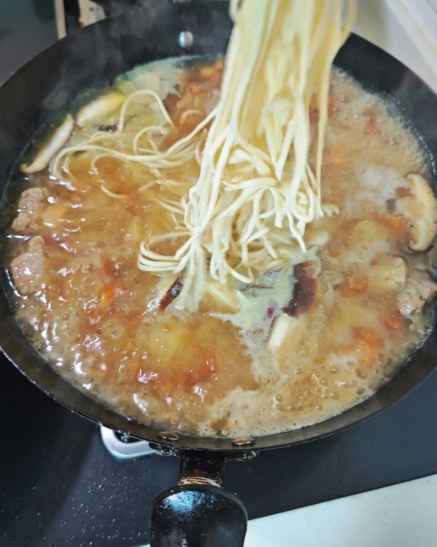 표고버섯 조각들이 가득한 닭고기 국물이 끓는 웍 속으로 하얗고 신선한 생면 한 뭉치를 넣는 모습