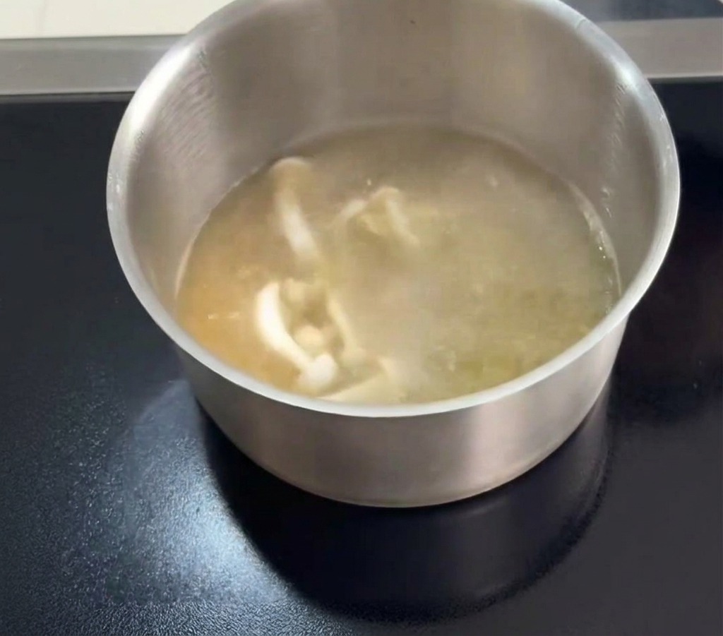 끓는 맑은 닭고기 육수에 백만송이버섯과 얇은 주황색 동충하초를 넣는 모습.