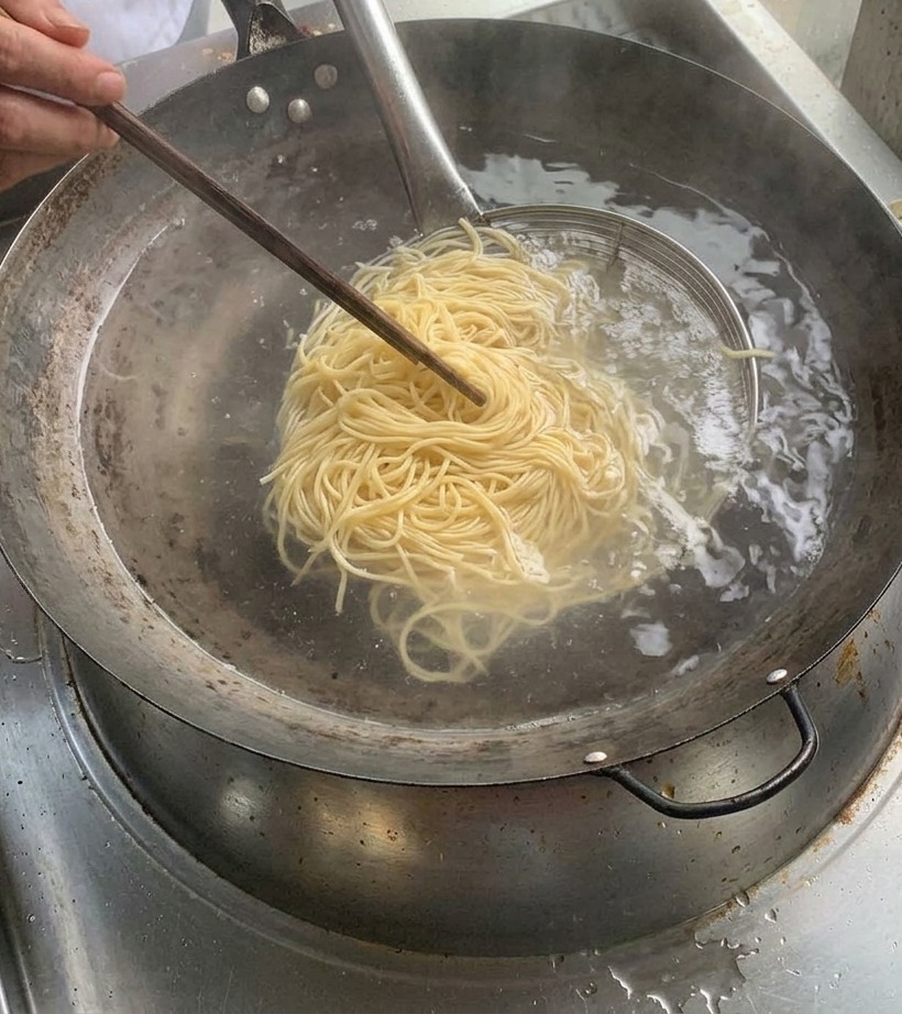 끓는 물 냄비 위로 금속 채반에 담겨 있는 잘 삶아진 면.
