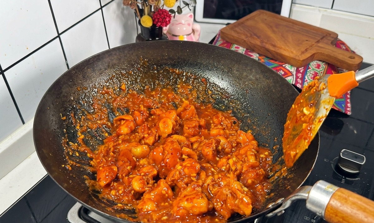 검은색 웍에서 요리용 주걱으로 보글보글 끓는 진한 빨간 양념 속의 닭고기 조각들을 계속 볶아주는 모습.