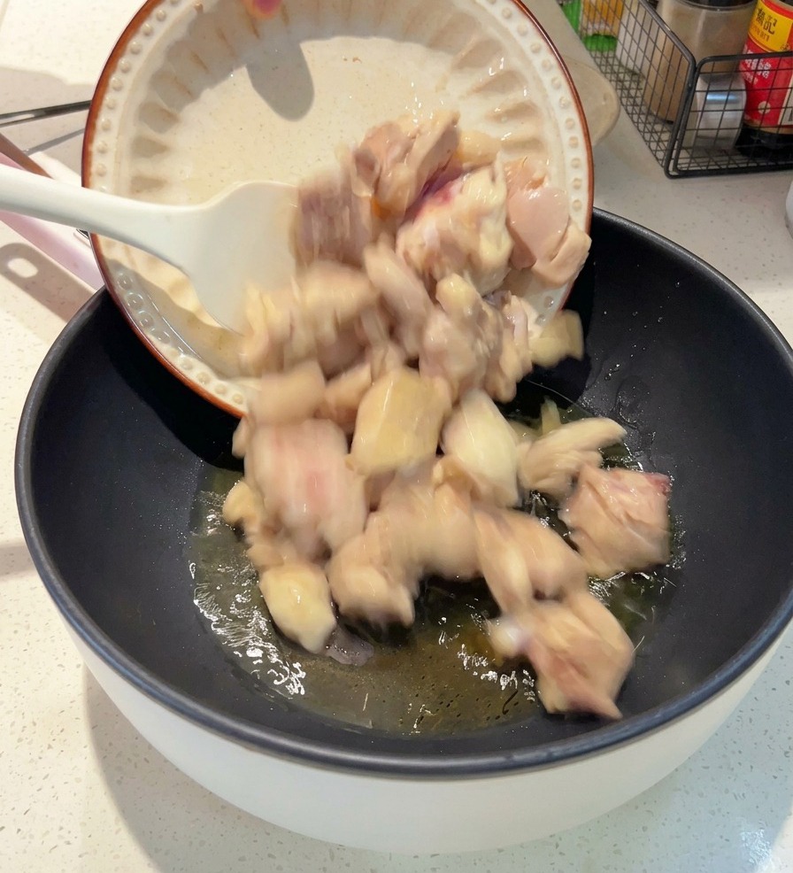 기름이 달구어진 어두운 팬에 흰 접시에 담긴 데친 닭고기 조각들을 넣는 모습