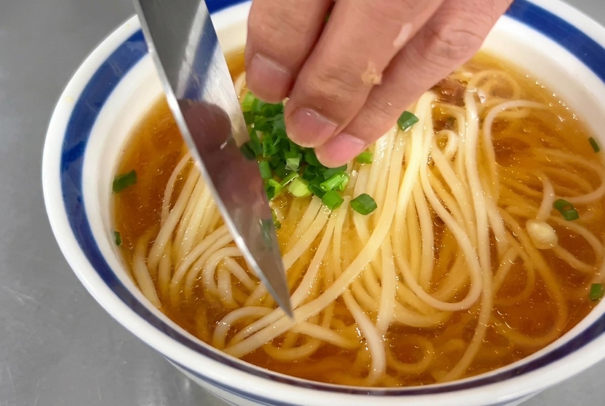 국수 그릇 위에 손으로 송송 썬 초록색 쪽파 고명을 뿌리는 모습