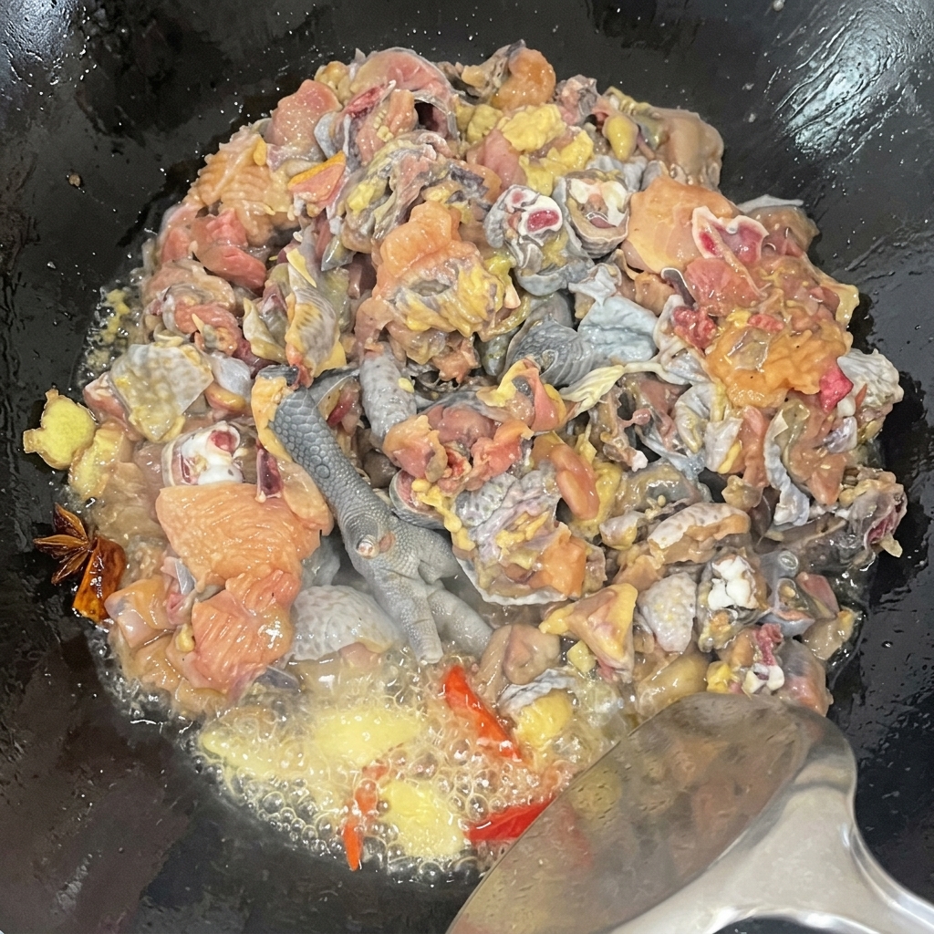 보글보글 끓는 기름과 양념 속에서 오골계 조각들을 웍에 넣고 빠르게 뒤섞는 근접 샷