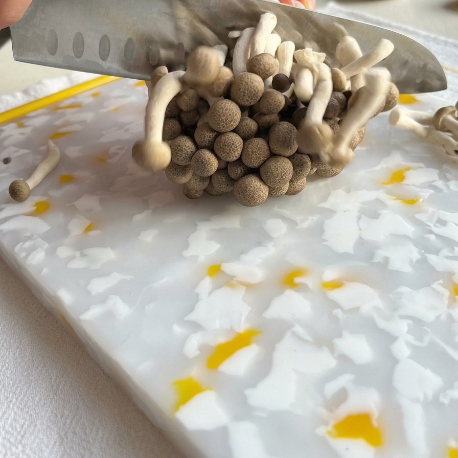 패턴 도마 위에서 주방 칼로 갈색 만가닥버섯 다발의 밑동을 자르는 모습.