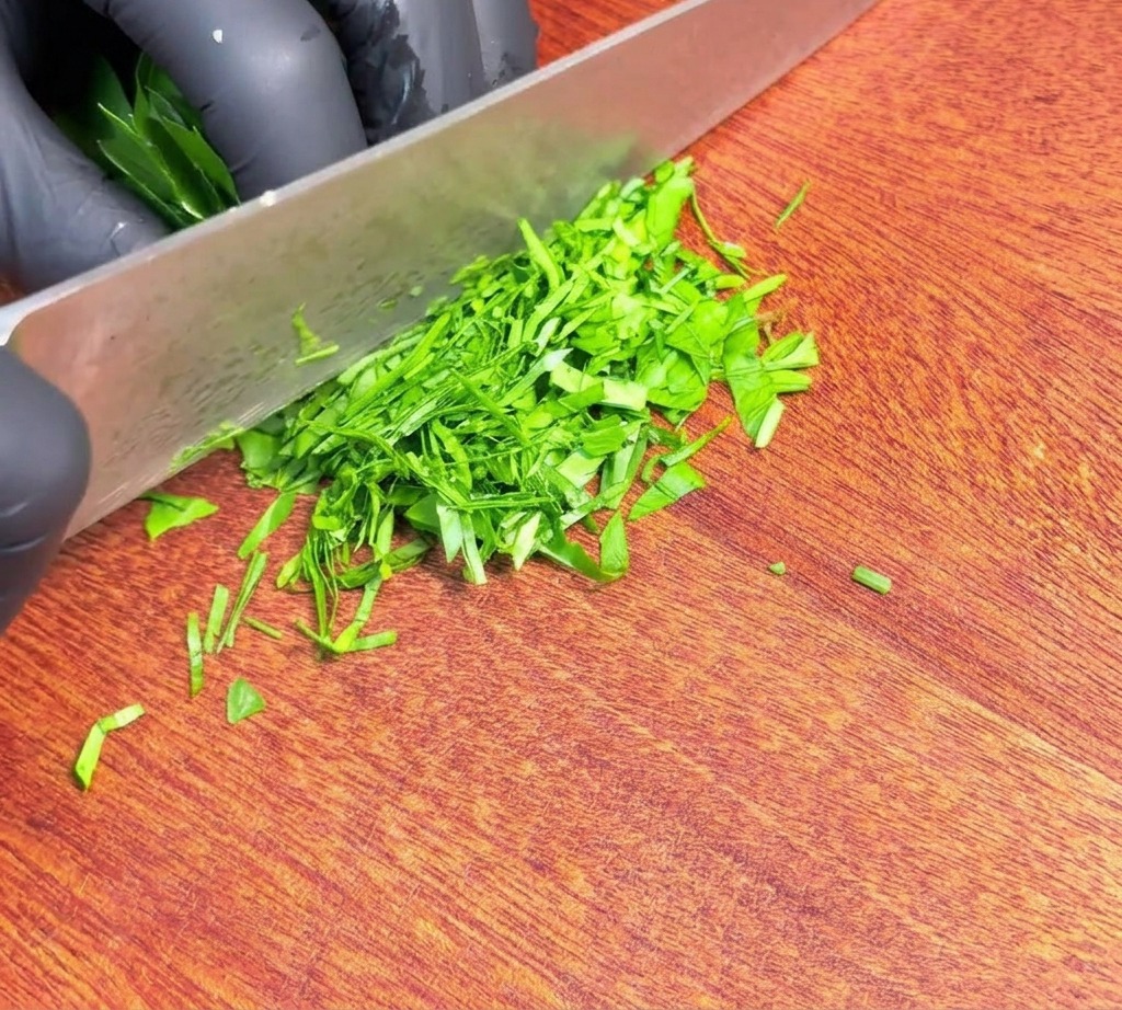 나무 도마 위에 날카로운 칼날과 함께 잘게 다져진 신선한 초록색 파슬리가 펼쳐져 있는 모습.