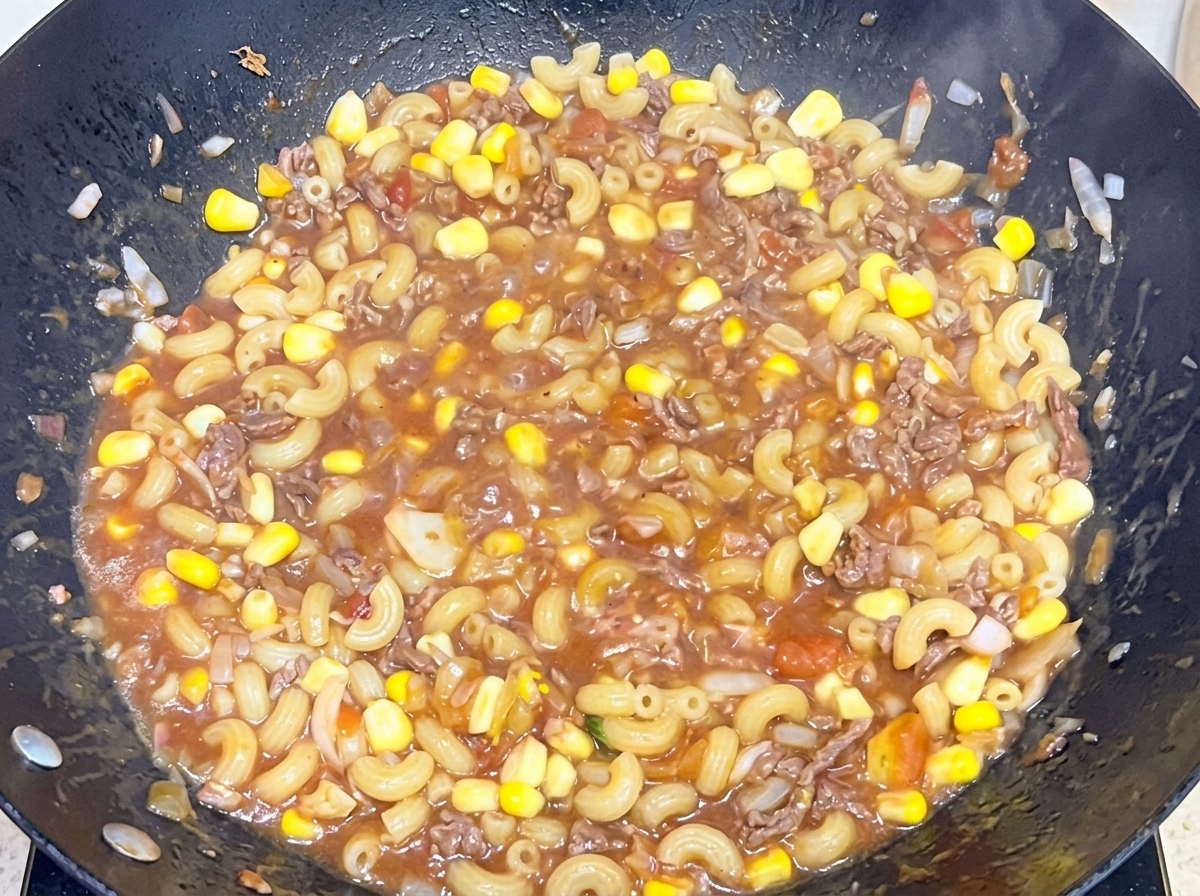 큰 웍 안에서 감칠맛 나는 소고기 토마토 소스에 삶은 마카로니를 넣고 섞는 모습