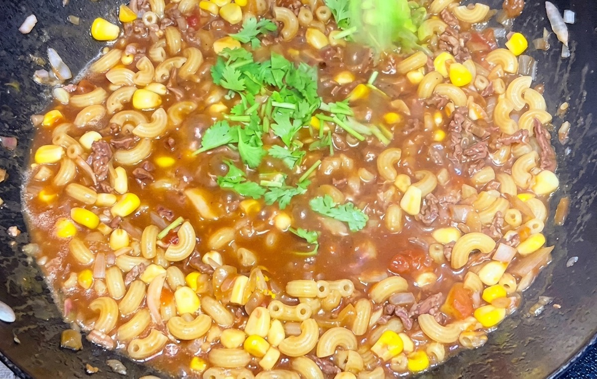 김이 모락모락 나는 소고기 토마토 마카로니 팬 위에 다진 초록색 고수를 뿌리는 손
