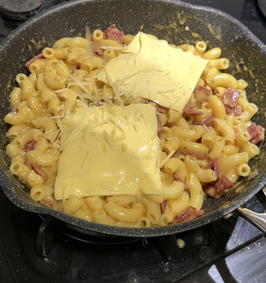 조리 중인 맥앤치즈 팬 윗면에 사각형 모양의 노란색 슬라이스 치즈 두 장과 눈꽃 모양의 슈레드 치즈가 소복이 얹어진 모습.