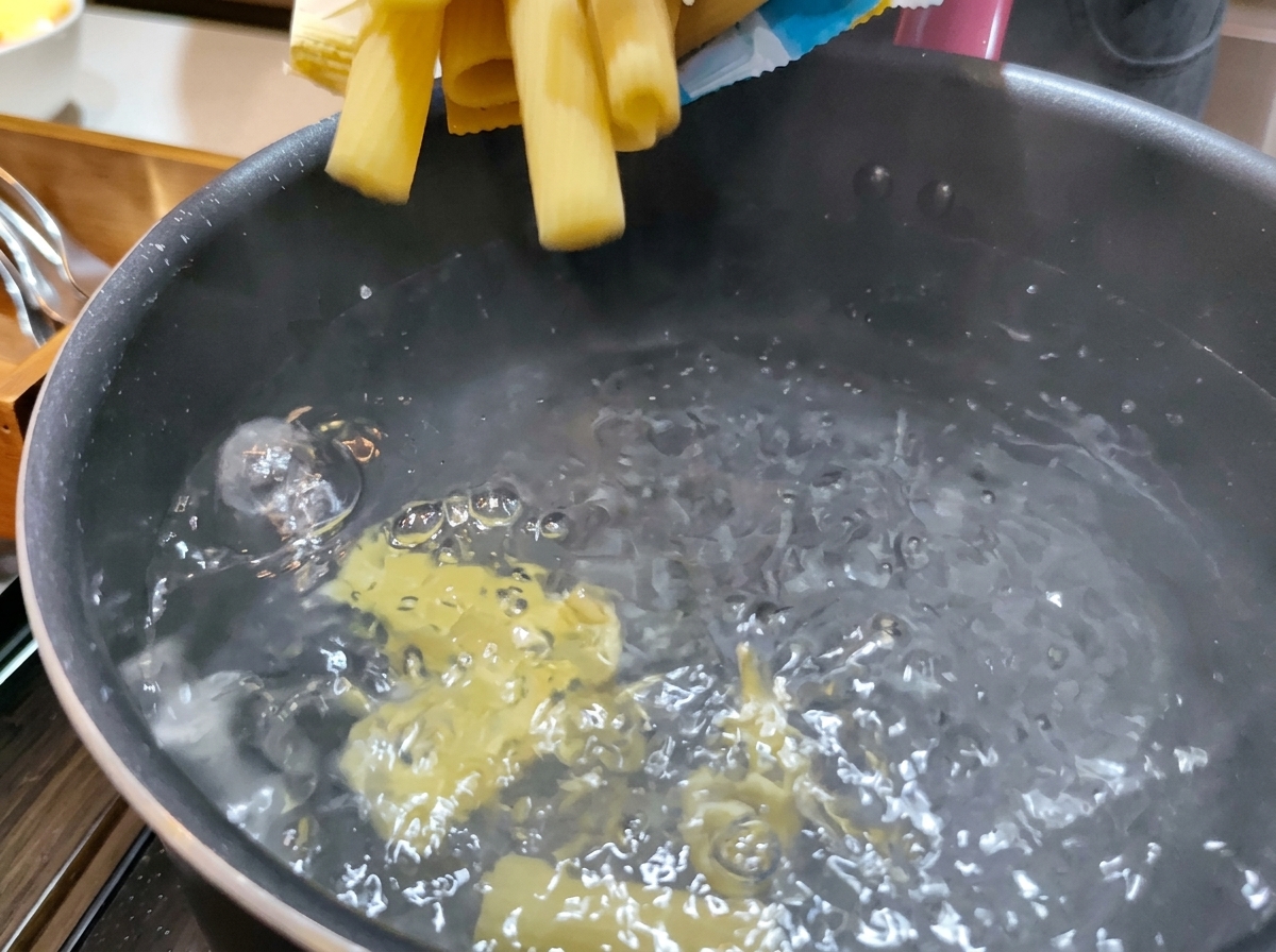 보글보글 끓어오르는 물이 담긴 냄비에 단단한 노란색 리카토니 파스타 면을 넣는 모습