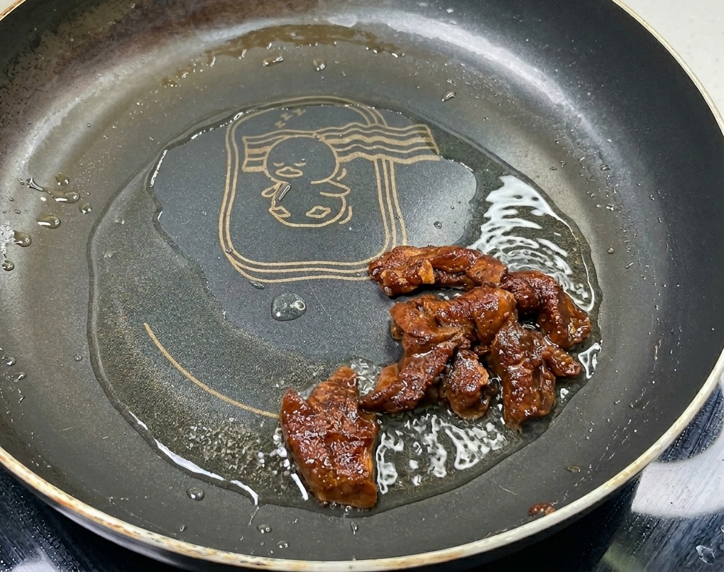 기름을 두른 팬에서 진한 갈색과 윤기를 띠며 노릇하게 볶아지고 있는 양념된 돼지고기 안심