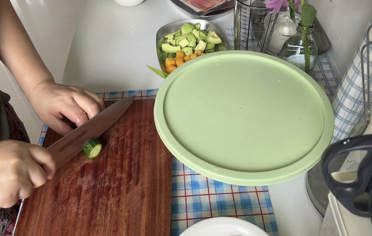 나무 도마 위에서 날카로운 칼로 신선한 오이를 얇고 둥글게 썰고 있는 모습.