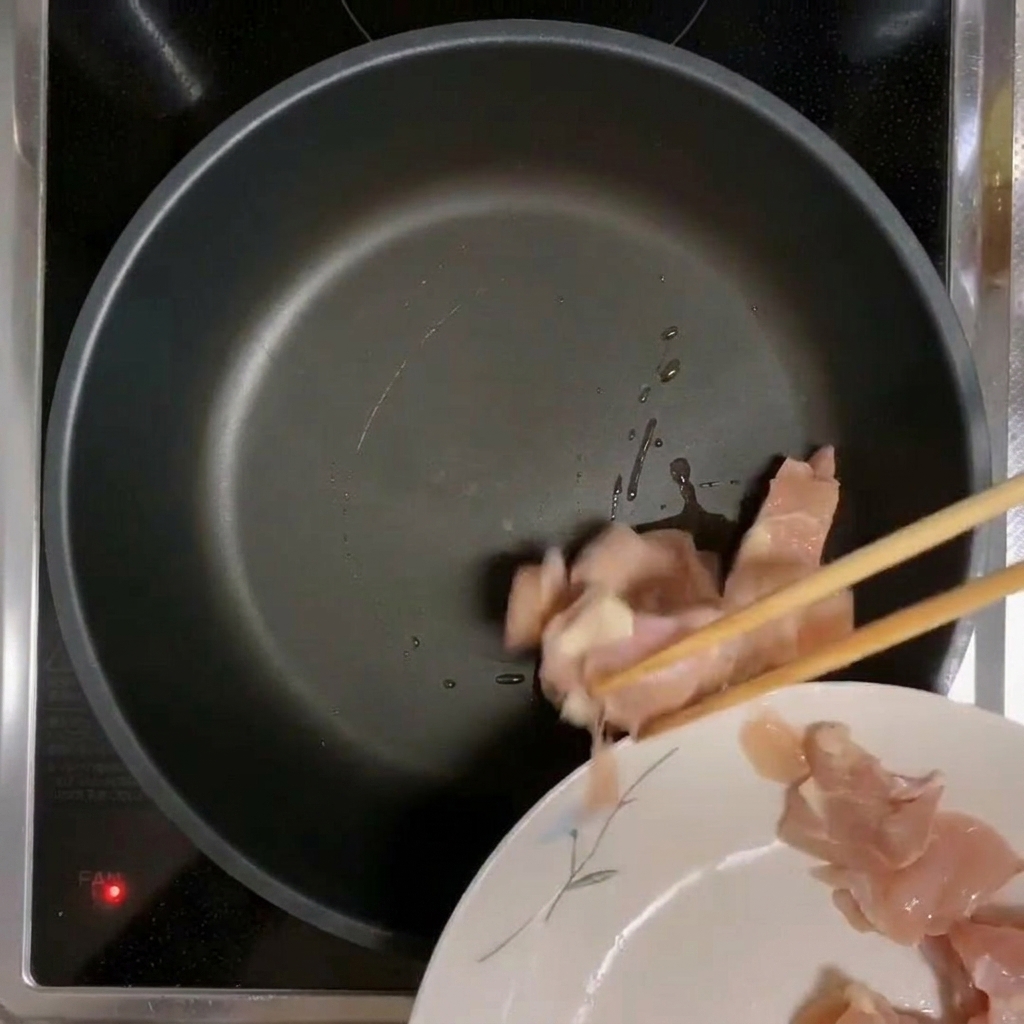 기름을 두르고 예열된 팬에 닭고기 조각을 넣는 모습.