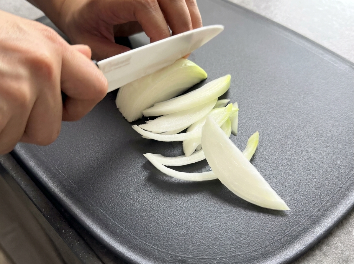 도마 위에서 반 개 분량의 양파를 얇게 채 썰고 있는 모습.