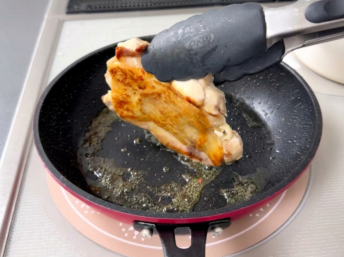 집게로 닭고기를 뒤집어 노릇하게 익은 껍질을 보여주는 모습.
