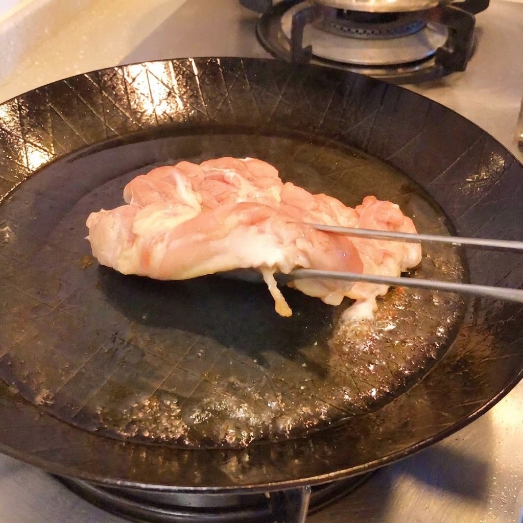집게로 닭고기 끝을 들어 올려 바삭한 황금빛 껍질을 확인하는 모습.