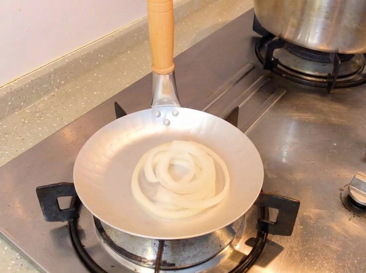 양파 링이 담긴 팬에 숟가락으로 간장 소스를 붓는 모습.